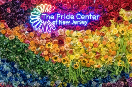 A backdrop of flowers in every color of the rainbow, with The Pride Center of New Jersey’s logo at the top